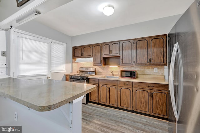 kitchen with stainless steel appliances, sink, backsplash, and light wood-type flooring