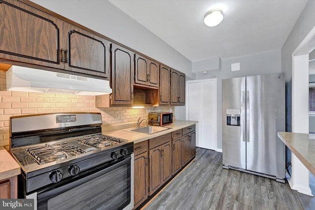 kitchen with dark wood-type flooring, black range with gas cooktop, sink, stainless steel fridge, and decorative backsplash