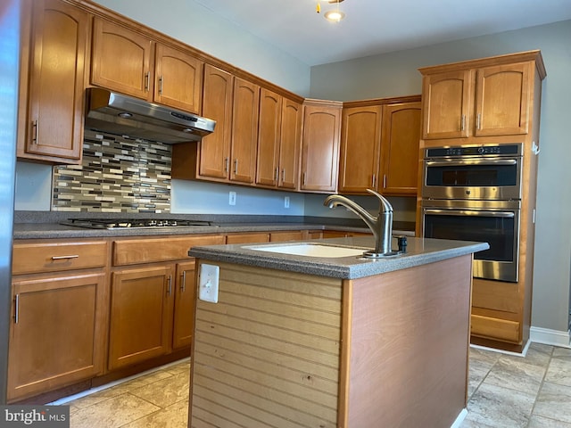 kitchen featuring decorative backsplash, sink, appliances with stainless steel finishes, and a center island with sink