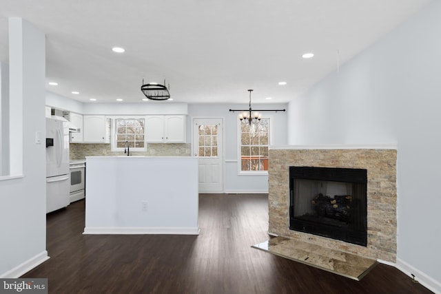 kitchen with white appliances, white cabinetry, hanging light fixtures, a fireplace, and decorative backsplash