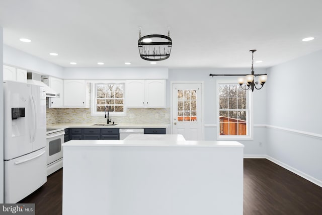 kitchen featuring pendant lighting, sink, white appliances, white cabinets, and a kitchen island