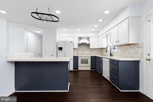 kitchen with sink, kitchen peninsula, white cabinets, white appliances, and wall chimney range hood