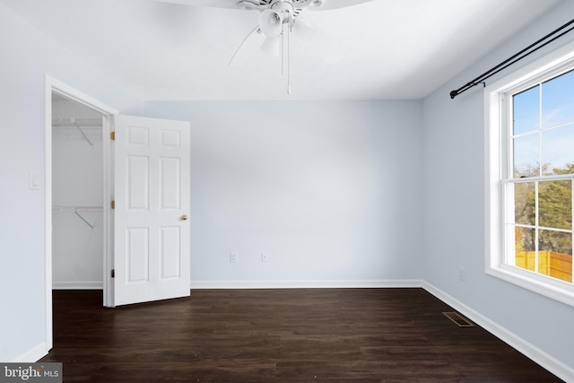 unfurnished bedroom with multiple windows, dark wood-type flooring, ceiling fan, and a closet