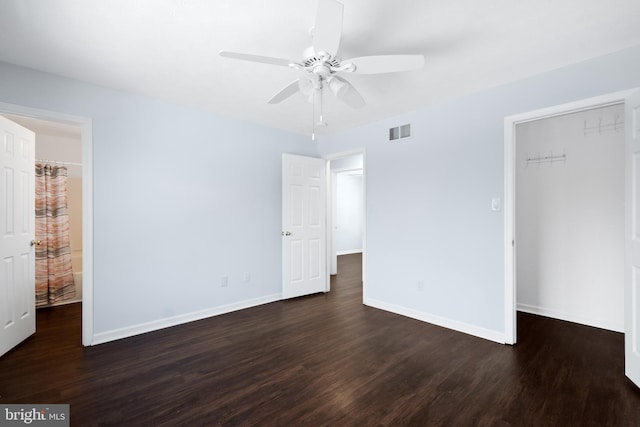 unfurnished bedroom with dark wood-type flooring, ceiling fan, a closet, and a walk in closet