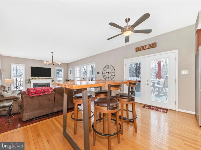 dining room with light wood-type flooring, ceiling fan with notable chandelier, and french doors