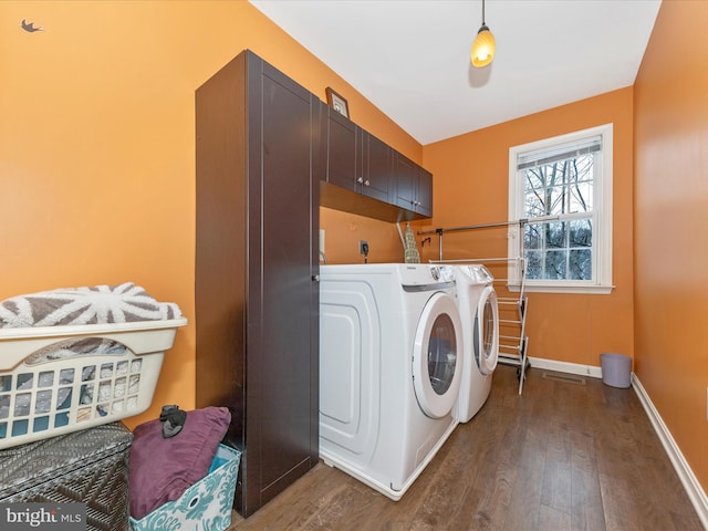 clothes washing area with cabinets, washing machine and dryer, and dark hardwood / wood-style flooring