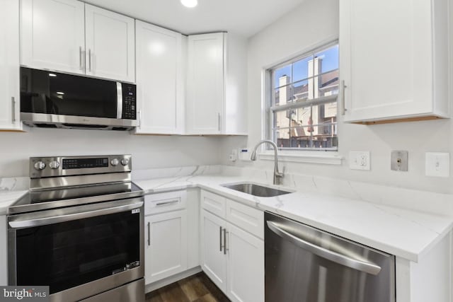 kitchen featuring appliances with stainless steel finishes, white cabinetry, sink, light stone counters, and dark wood-type flooring