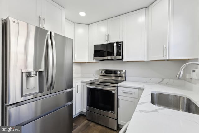 kitchen with light stone counters, stainless steel appliances, sink, and white cabinets