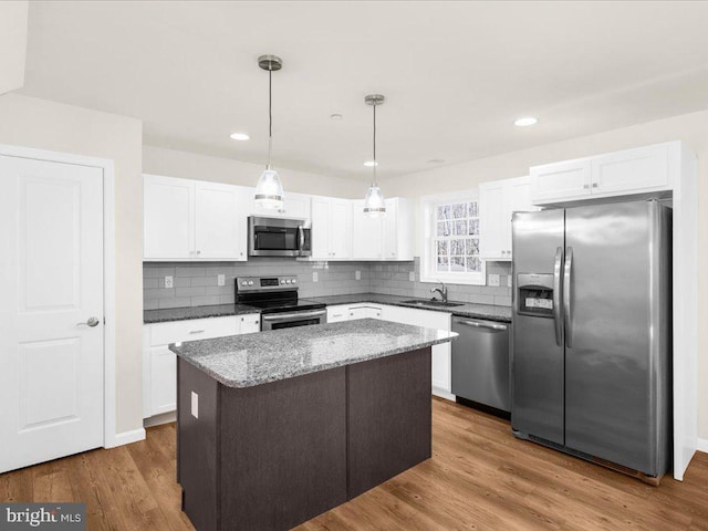 kitchen featuring white cabinetry, hanging light fixtures, dark stone countertops, a kitchen island, and stainless steel appliances