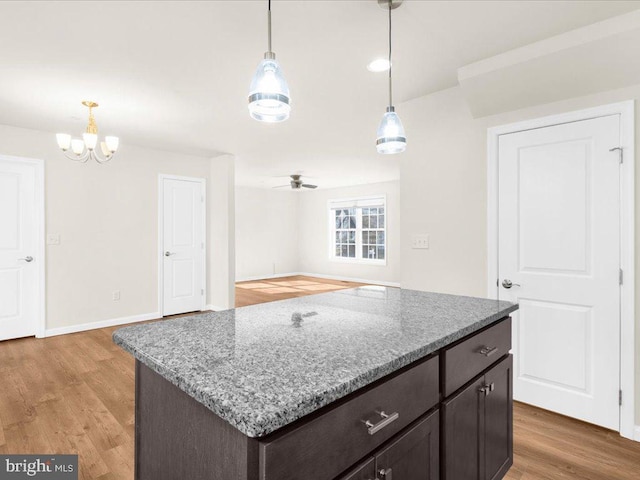 kitchen featuring a kitchen island, decorative light fixtures, hardwood / wood-style flooring, light stone counters, and dark brown cabinetry