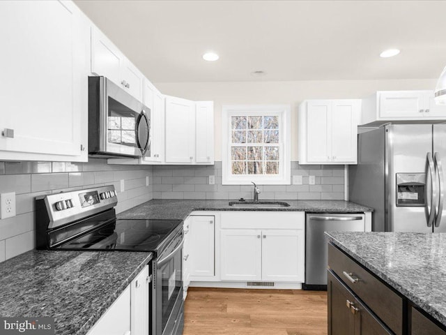 kitchen with dark stone countertops, stainless steel appliances, sink, and white cabinets