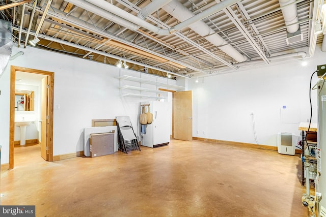 basement with a sink, freestanding refrigerator, and baseboards