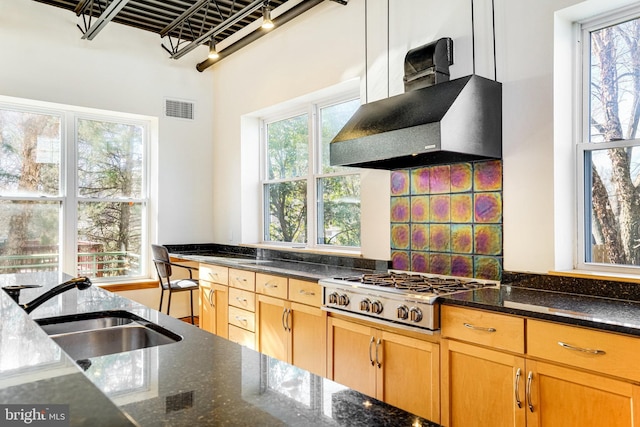 kitchen featuring visible vents, wall chimney exhaust hood, dark stone countertops, stainless steel gas cooktop, and a sink