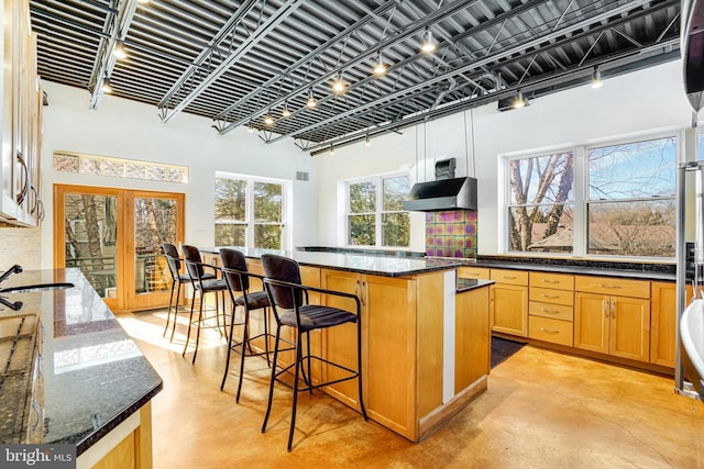 kitchen featuring exhaust hood, finished concrete flooring, french doors, a center island, and dark stone counters