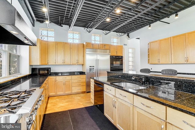 kitchen with a towering ceiling, wall chimney range hood, light brown cabinetry, black appliances, and a sink