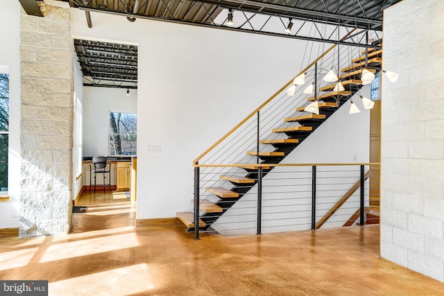 staircase with concrete block wall, a towering ceiling, and finished concrete floors