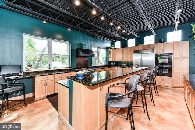 kitchen featuring a kitchen island, concrete flooring, dark stone counters, under cabinet range hood, and built in refrigerator