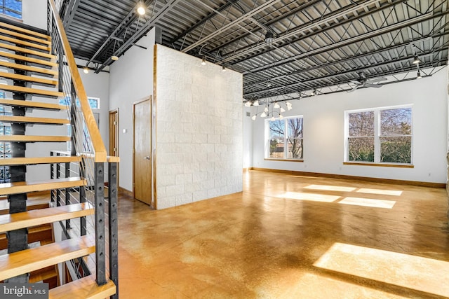 interior space featuring finished concrete flooring, stairs, baseboards, and a high ceiling