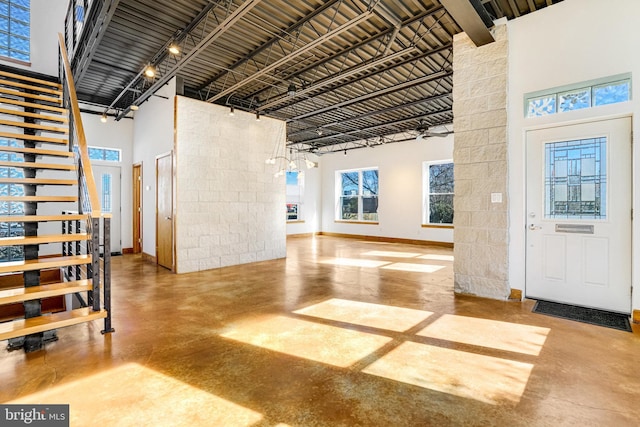 entryway with concrete flooring, a towering ceiling, baseboards, stairs, and track lighting