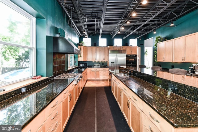 kitchen with stainless steel appliances, a high ceiling, wall chimney exhaust hood, and light brown cabinetry