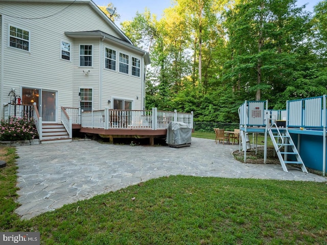 back of property featuring a wooden deck, a yard, a patio area, and a playground