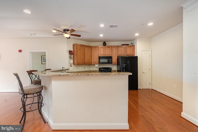 kitchen featuring a breakfast bar, kitchen peninsula, light hardwood / wood-style floors, and black appliances