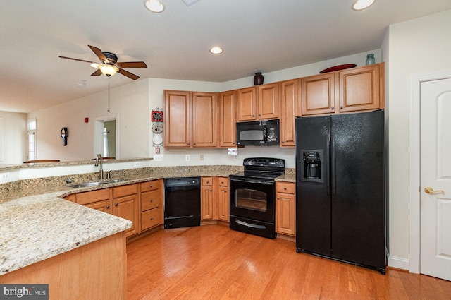 kitchen with sink, black appliances, light stone countertops, and light wood-type flooring