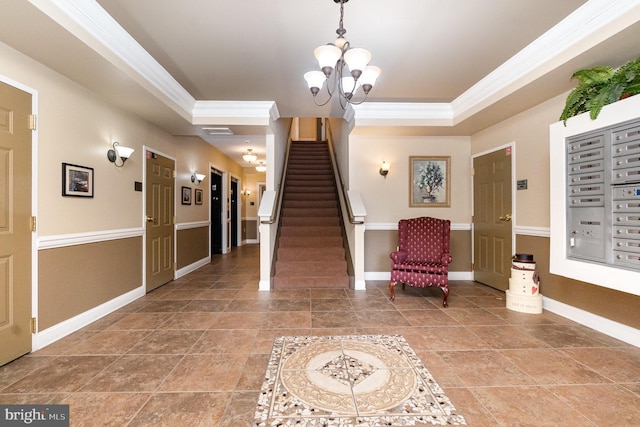 tiled entryway featuring ornamental molding, a tray ceiling, a chandelier, and a mail area