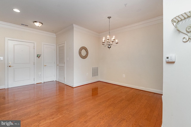 spare room featuring ornamental molding, hardwood / wood-style floors, and an inviting chandelier