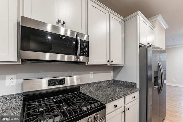 kitchen featuring crown molding, appliances with stainless steel finishes, dark stone counters, light hardwood / wood-style floors, and white cabinets