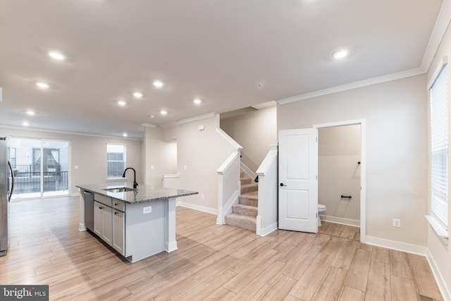 kitchen with sink, stainless steel appliances, light hardwood / wood-style floors, an island with sink, and stone countertops