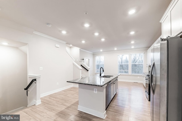 kitchen featuring appliances with stainless steel finishes, dark stone countertops, white cabinets, a center island with sink, and light wood-type flooring