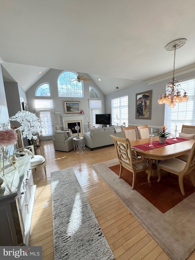 dining area with ceiling fan with notable chandelier, light hardwood / wood-style flooring, and high vaulted ceiling