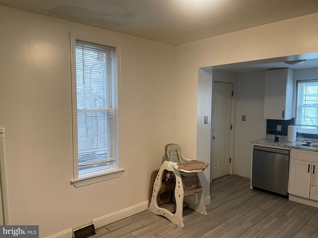 kitchen with white cabinetry, sink, stainless steel dishwasher, light stone counters, and light hardwood / wood-style flooring