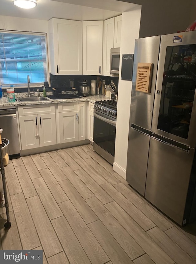 kitchen with appliances with stainless steel finishes, white cabinetry, sink, decorative backsplash, and light stone counters