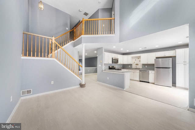 kitchen with appliances with stainless steel finishes, a towering ceiling, white cabinetry, sink, and light hardwood / wood-style flooring