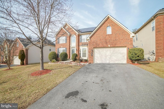 view of front of house featuring driveway, a garage, solar panels, a front lawn, and brick siding