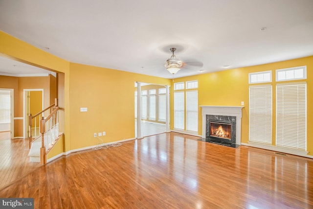 unfurnished living room featuring stairway, a premium fireplace, a ceiling fan, wood finished floors, and baseboards