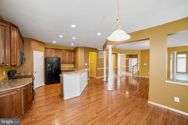 kitchen with decorative columns, brown cabinetry, light wood-style floors, a center island, and black appliances