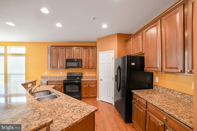 kitchen featuring light wood finished floors, light stone countertops, black appliances, a sink, and recessed lighting