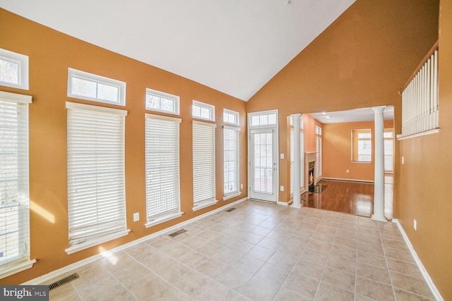 tiled empty room featuring decorative columns, visible vents, baseboards, a lit fireplace, and high vaulted ceiling