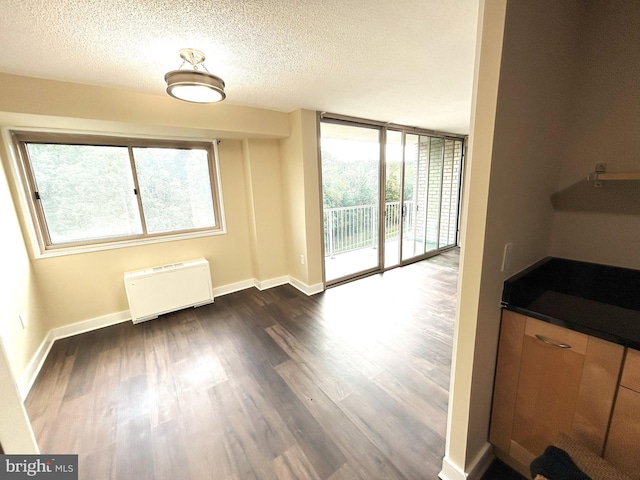 unfurnished dining area with dark wood-type flooring, a textured ceiling, radiator, and expansive windows