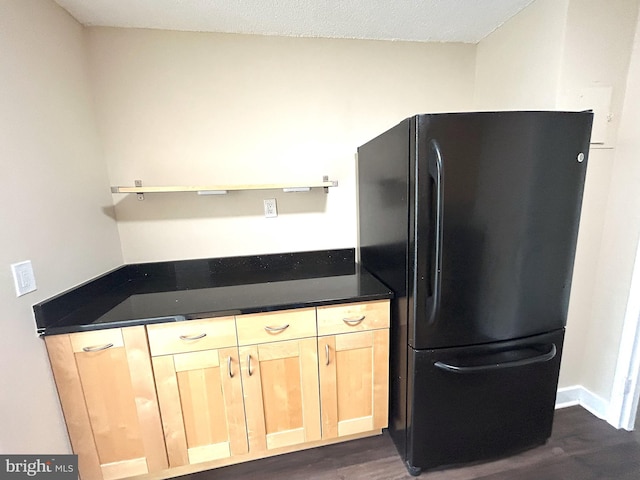 kitchen with light brown cabinetry, black fridge, dark wood-type flooring, and a textured ceiling