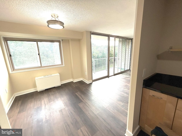 unfurnished dining area featuring dark wood-type flooring, a textured ceiling, radiator, and expansive windows