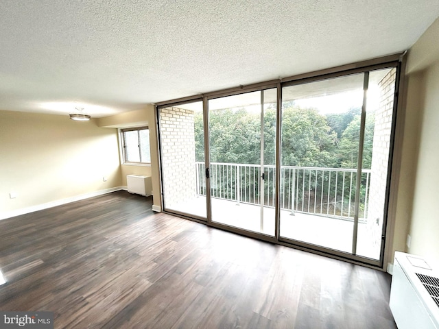 empty room with expansive windows, dark wood-type flooring, and a textured ceiling