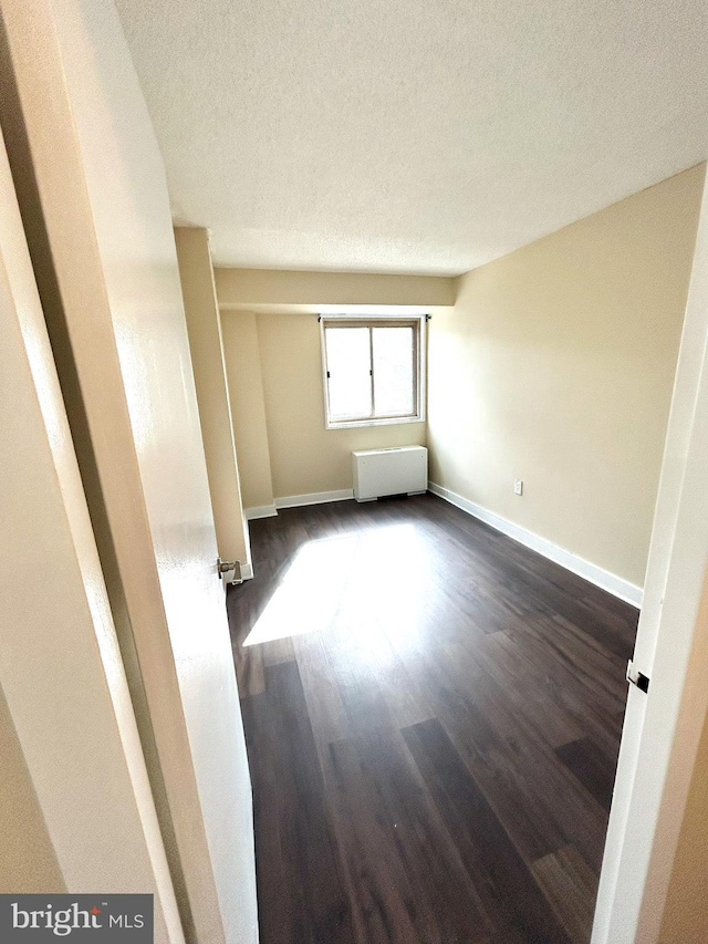 spare room with radiator, a textured ceiling, and dark hardwood / wood-style flooring