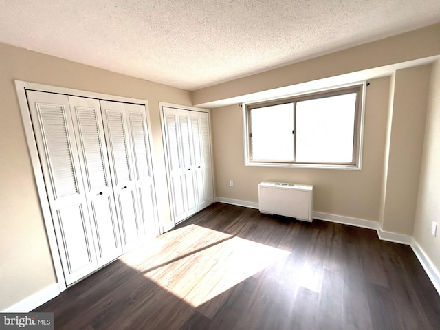 unfurnished bedroom with dark wood-type flooring, a textured ceiling, and multiple closets