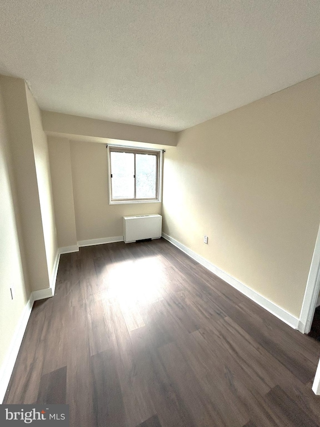 spare room featuring radiator heating unit, a textured ceiling, and dark hardwood / wood-style floors