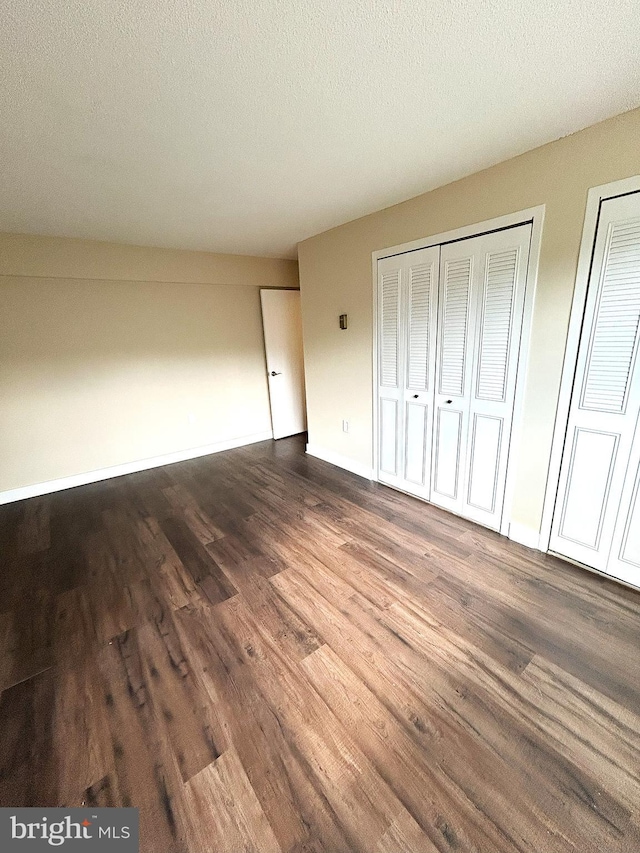 unfurnished bedroom with multiple closets, a textured ceiling, and dark hardwood / wood-style flooring