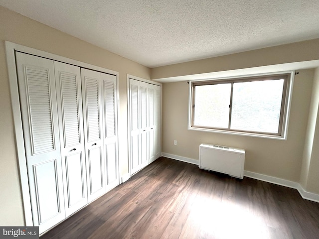 unfurnished bedroom featuring multiple closets, a textured ceiling, dark hardwood / wood-style floors, and radiator heating unit